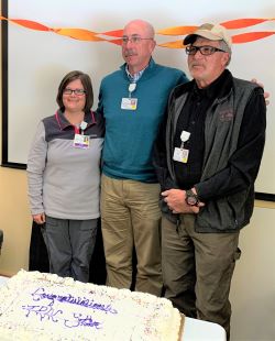 Molli Buchanan stands in front of cake with two men
